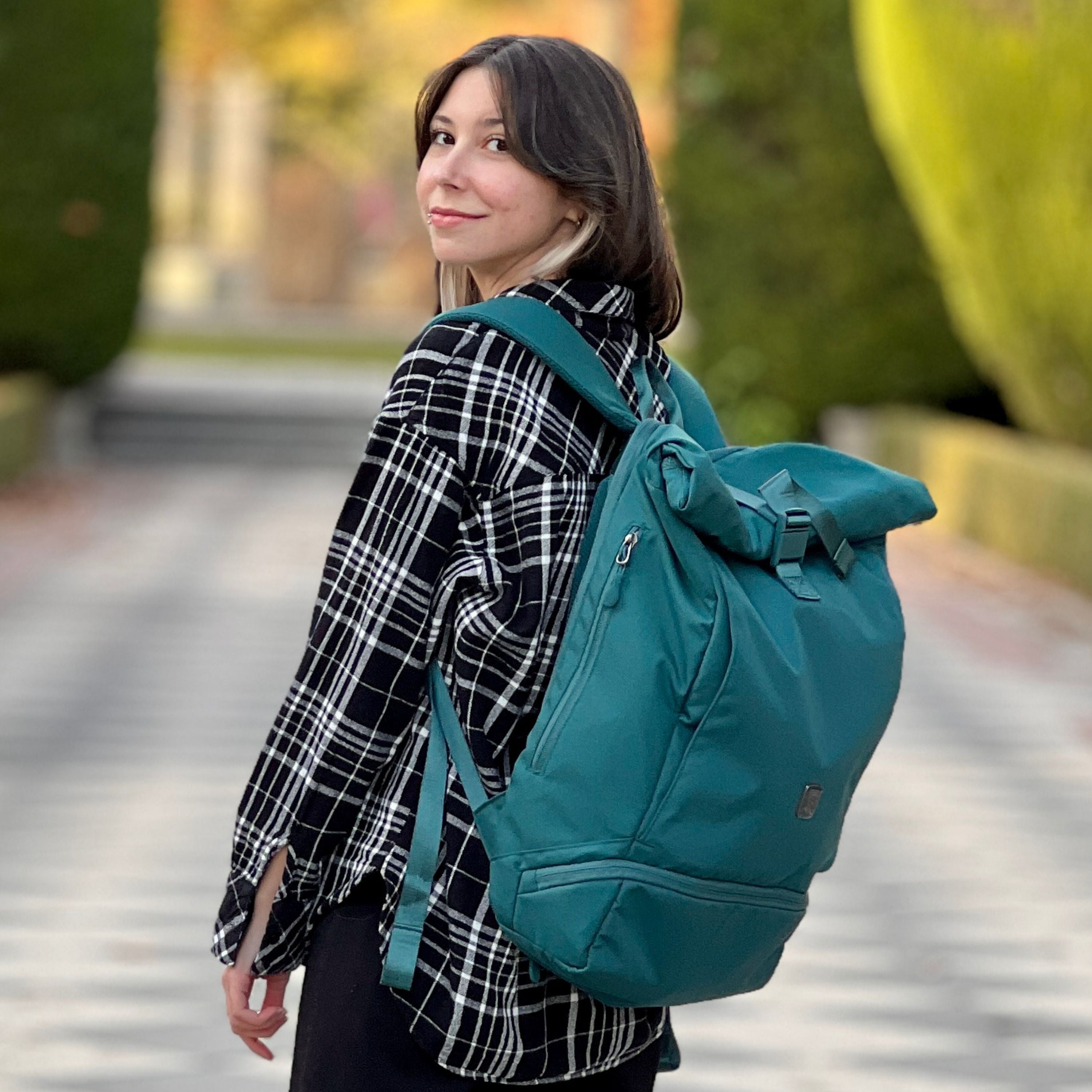 Frau traegt den FUCHS und REBELL EDDIE Rolltop Rucksack in petrolblau.