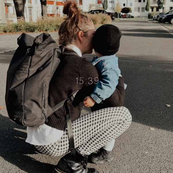 Junge Mutter umarmt ihr Kleinkind und traegt den schwarzen FUCHS & REBELL PIET Rolltop Rucksack